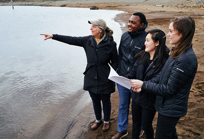 students and professor stand beside body of water