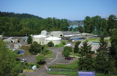 aerial view of industrial buildings near woods and a river with bridge