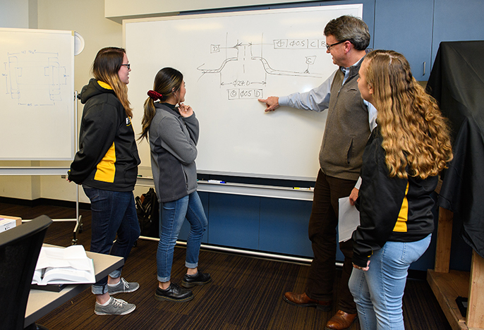 photo of students and professor around whiteboard